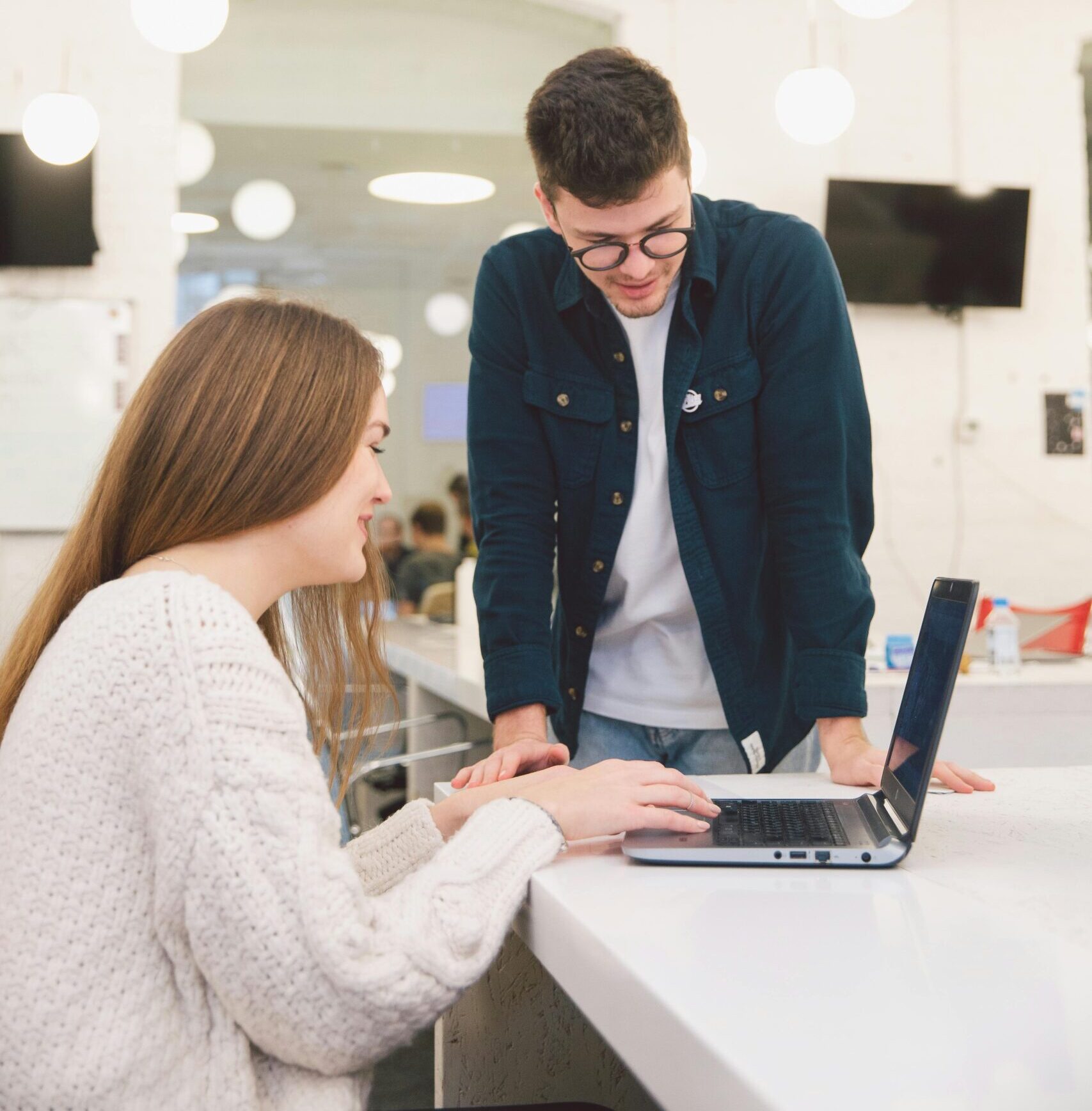 Two young adults collaborating over a laptop in a modern, bright office setting.